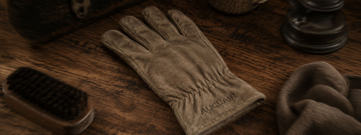 A single brown leather glove lies on a dark wooden surface, with the cuff showing the brand name 'AUGUSTUS' embroidered in dark thread.