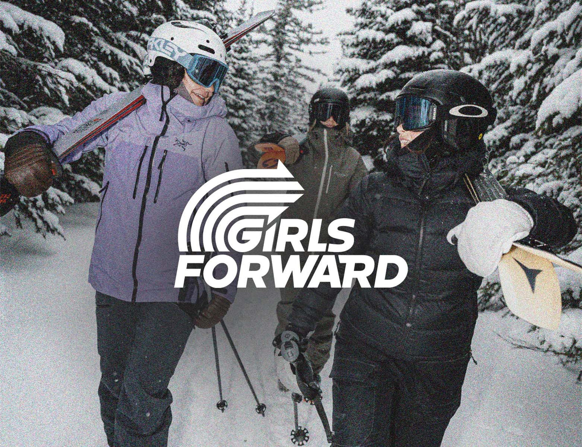 Three skiers in a snowy forest setting, wearing helmets, goggles, and ski jackets, with a large white 'GIRLS FORWARD' logo overlay in the center.