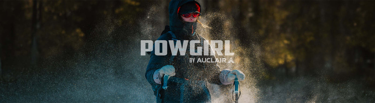 A person in winter gear stands outdoors in a snowy, dusty environment, wearing a dark hooded jacket, gloves, and red-tinted goggles. Large overlaid text reads 'POW GIRL BY AUCLAIR &'.